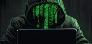 Hacker en hoodie devant un ordinateur avec du code vert pour illustrer une cyberattaque Cryptolocker.